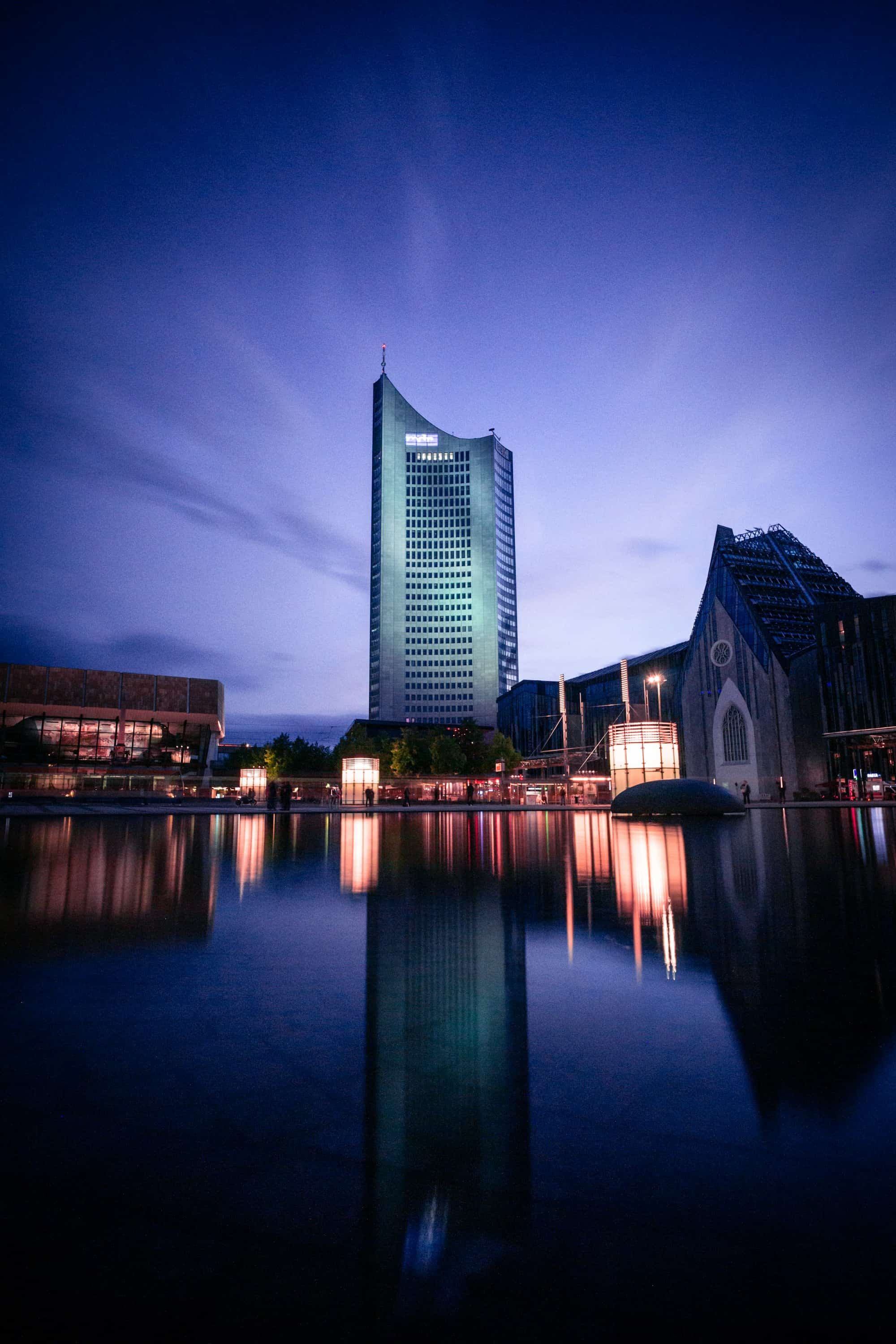 Das City-Hochhaus und das Paulinum am Augustusplatz zur blauen Stunde, gespiegelt im Wasserbecken